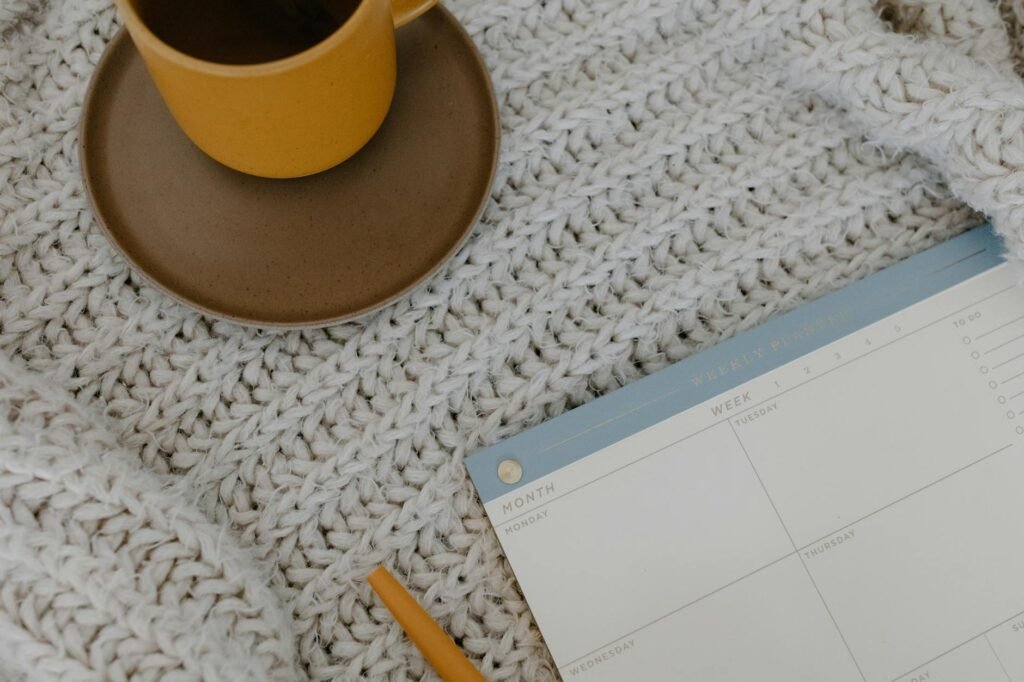 A weekly planner on a desk next to a calculator, coffee mug, and a few bills